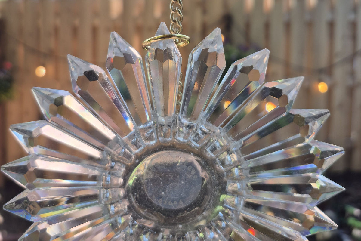 close up of handmade prism suncatcher with light on a fence behind it