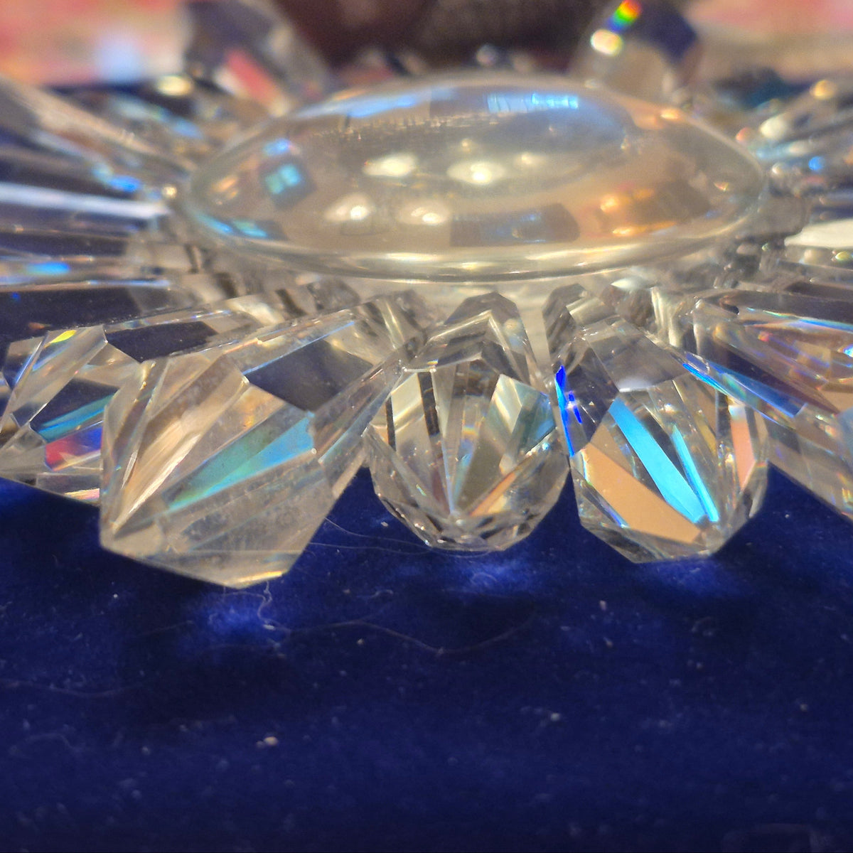 A clear faceted crystal prism suncatcher with a glass dome for engraving, all resting on a dark blue velvet surface with a blurred background.