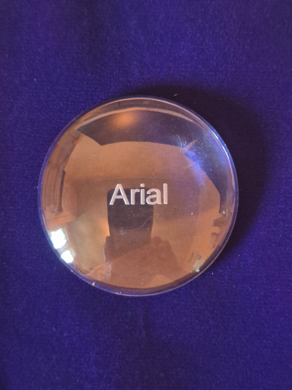 round glass disk on blue background with the word Arial engraved in middle