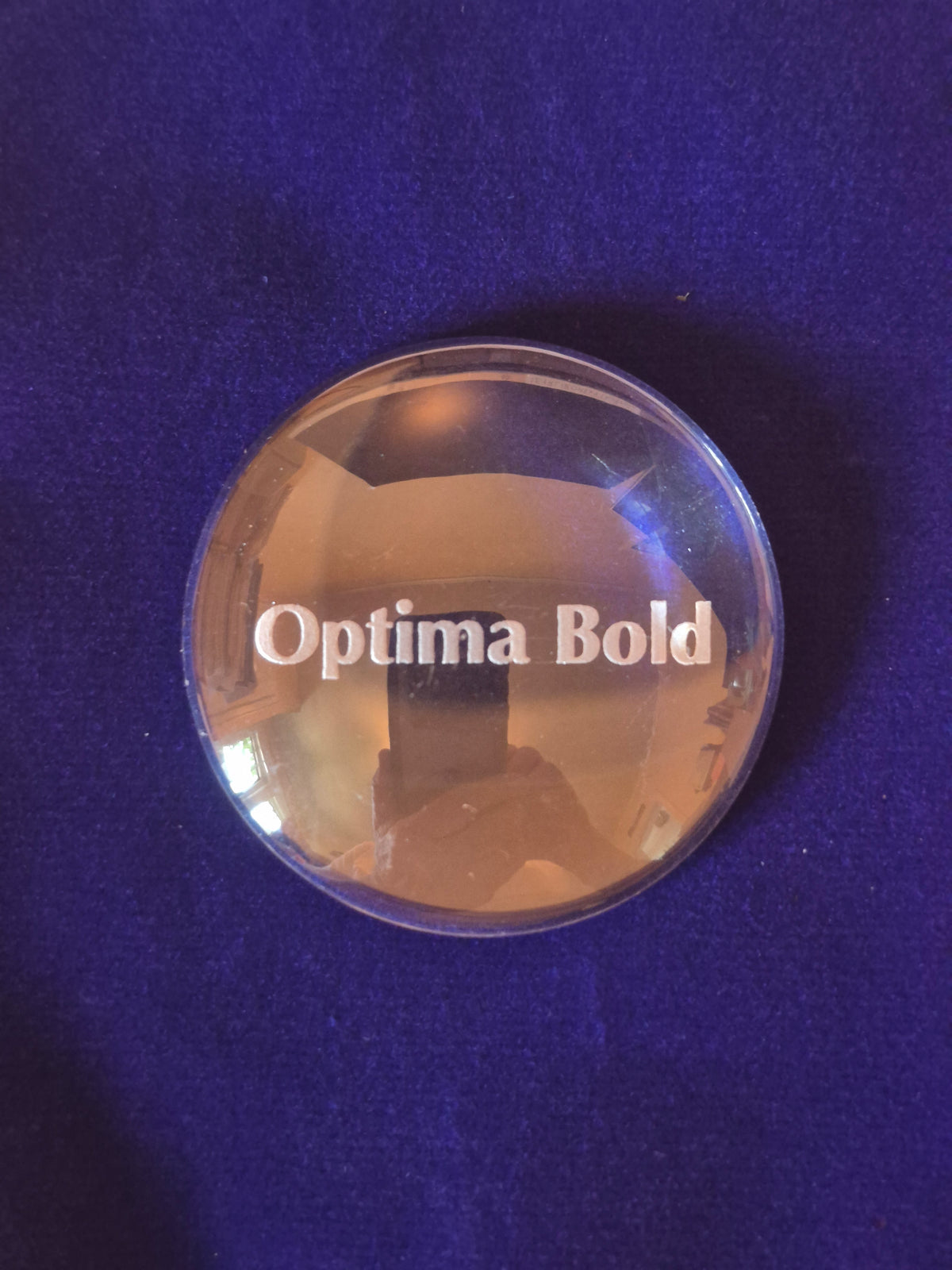 round glass disk on blue background with the word Optima Bold engraved in middle