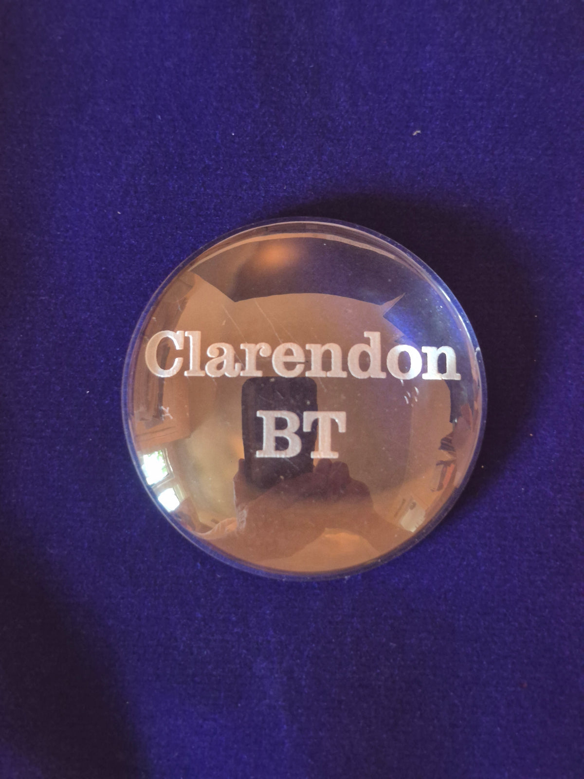 round glass disk on blue background with the word Clarendon BT engraved in middle