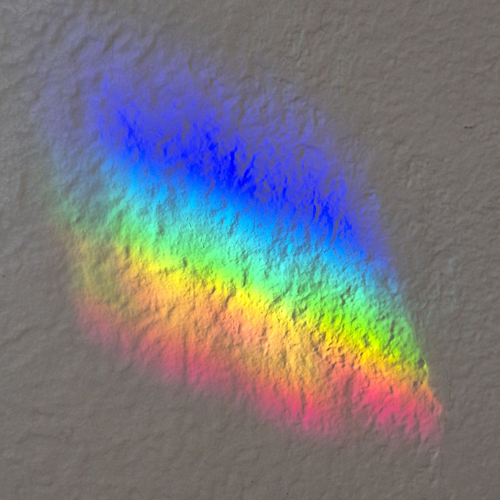 A rainbow light patch on a textured gray wall, displaying a smooth gradient of blue, green, yellow, orange, and pink light.