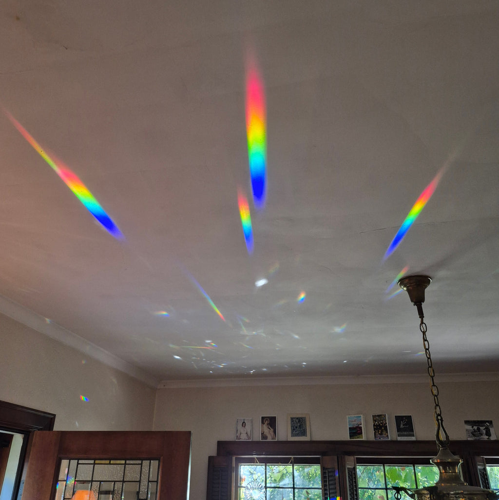 long rainbow spectrums projected onto dining room ceiling from hexagon prism suncatcher hanging in sunny window