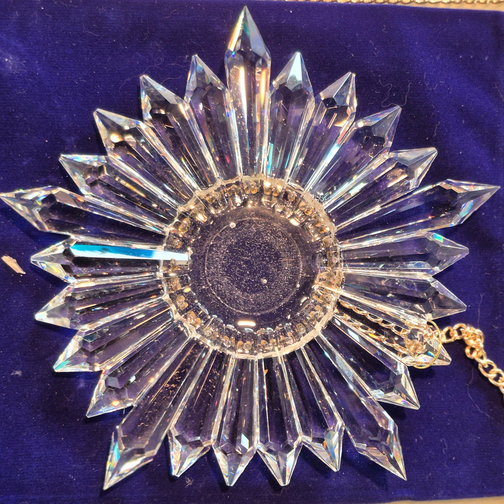 A clear faceted starburst crystal suncatcher with a gold-tone chain, displayed on a deep blue velvet pouch.