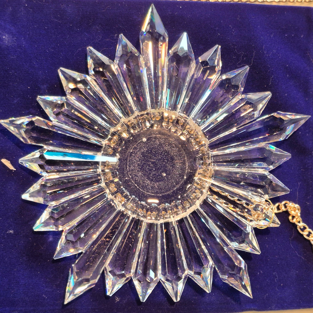 A clear faceted starburst crystal suncatcher with a gold-tone chain, displayed on a deep blue velvet pouch.