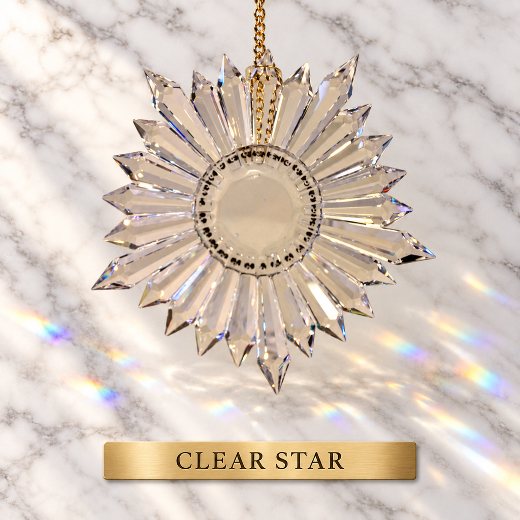 A clear faceted star-shaped lead crystal prism ornament with a gold hanging chain, shown against a white marble background with rainbow light reflections. A gold label at the bottom reads 'CLEAR STAR'.