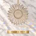 A clear faceted 6-inch diameter prism suncatcher with a gold hanging chain, shown against a white marble background with rainbow light reflections. A gold label at the bottom reads 'CLEAR 6-INCH'.