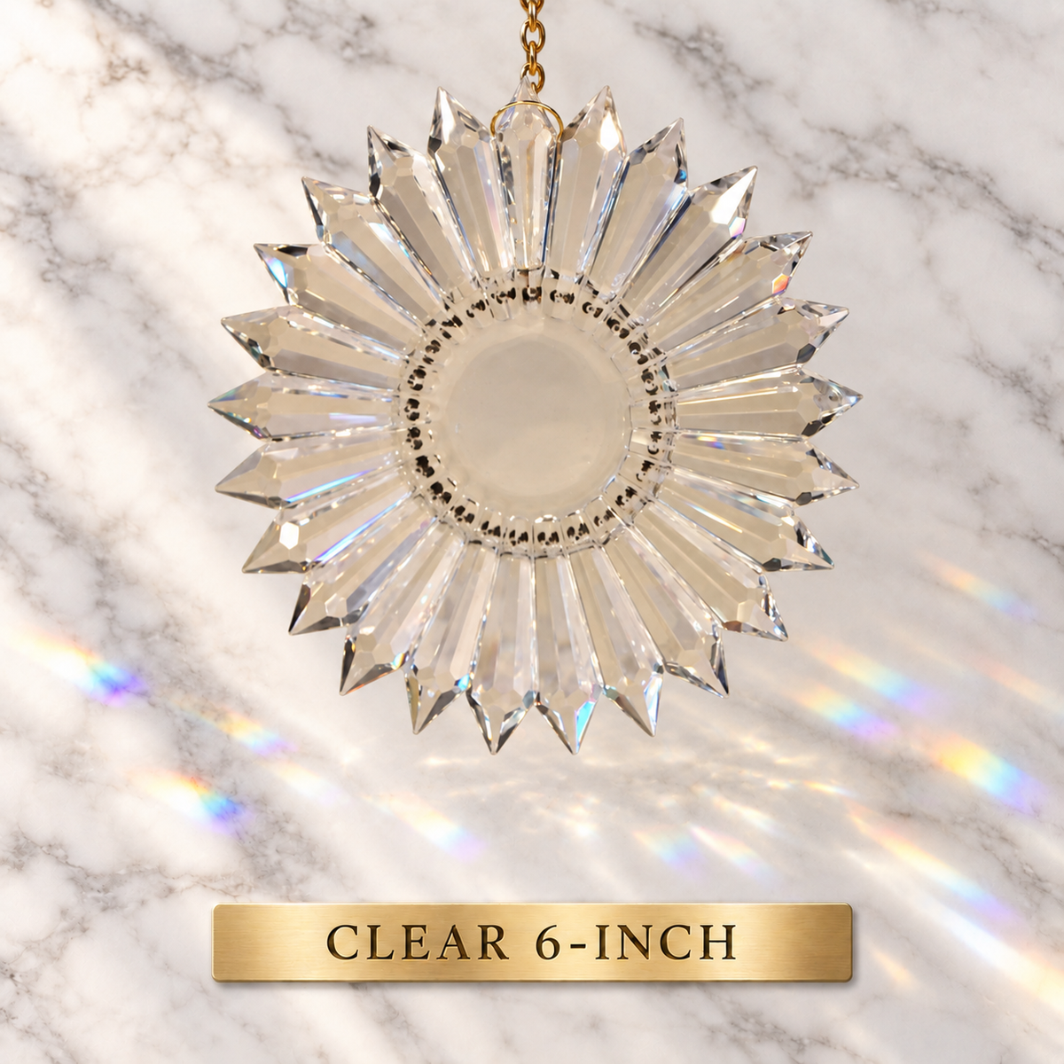 A clear faceted 6-inch diameter prism suncatcher with a gold hanging chain, shown against a white marble background with rainbow light reflections. A gold label at the bottom reads 'CLEAR 6-INCH'.