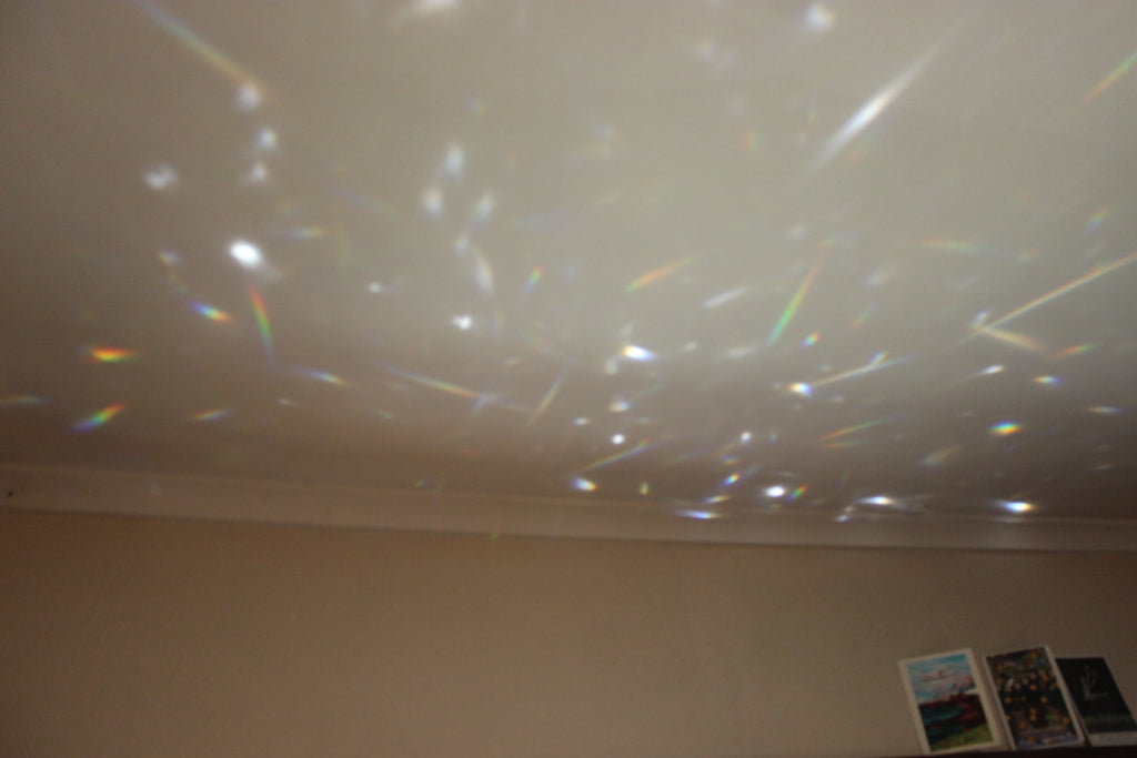 A prismatic refractor casting a field of rainbow light leaks and starry speckles onto a beige wall and ceiling.