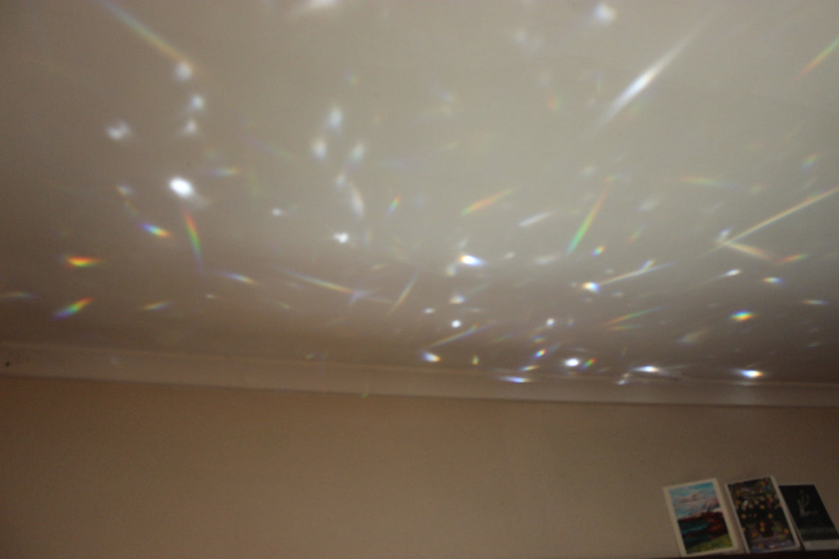 A prismatic refractor casting a field of rainbow light leaks and starry speckles onto a beige wall and ceiling.