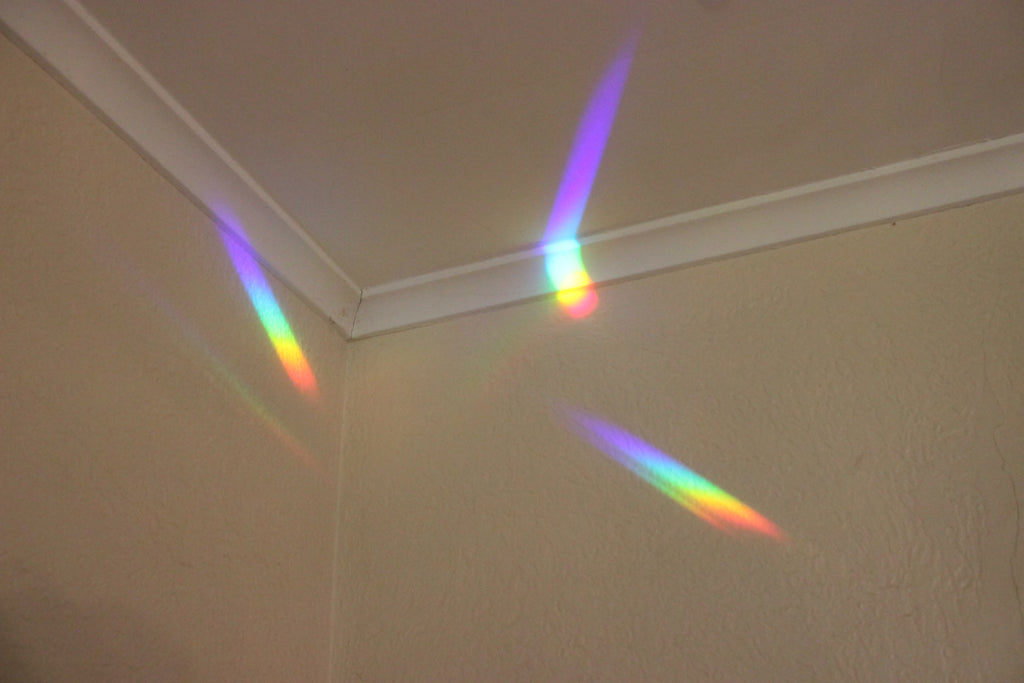 A rainbow light prism reflecting off the corner of a beige wall and white ceiling trim.