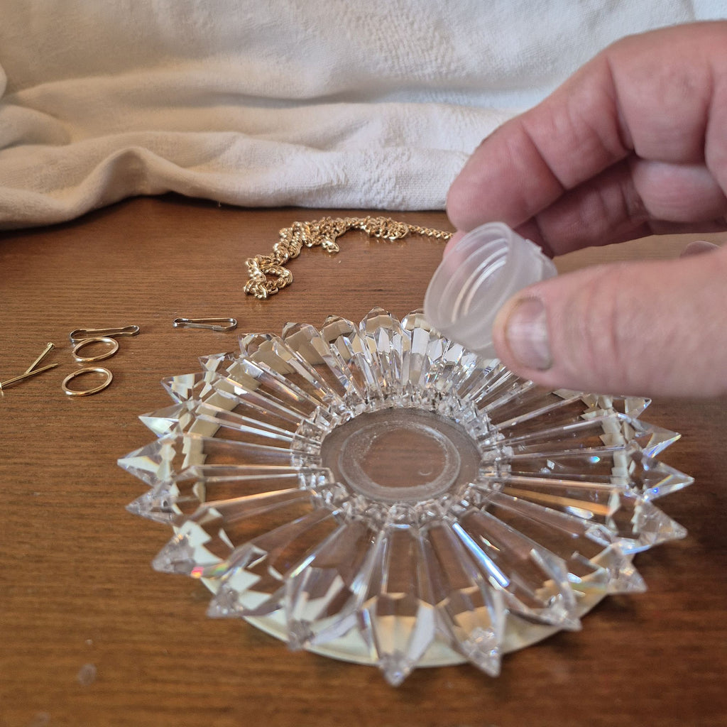 a hand pouring liquid epoxy resin into center well of prism suncatcher