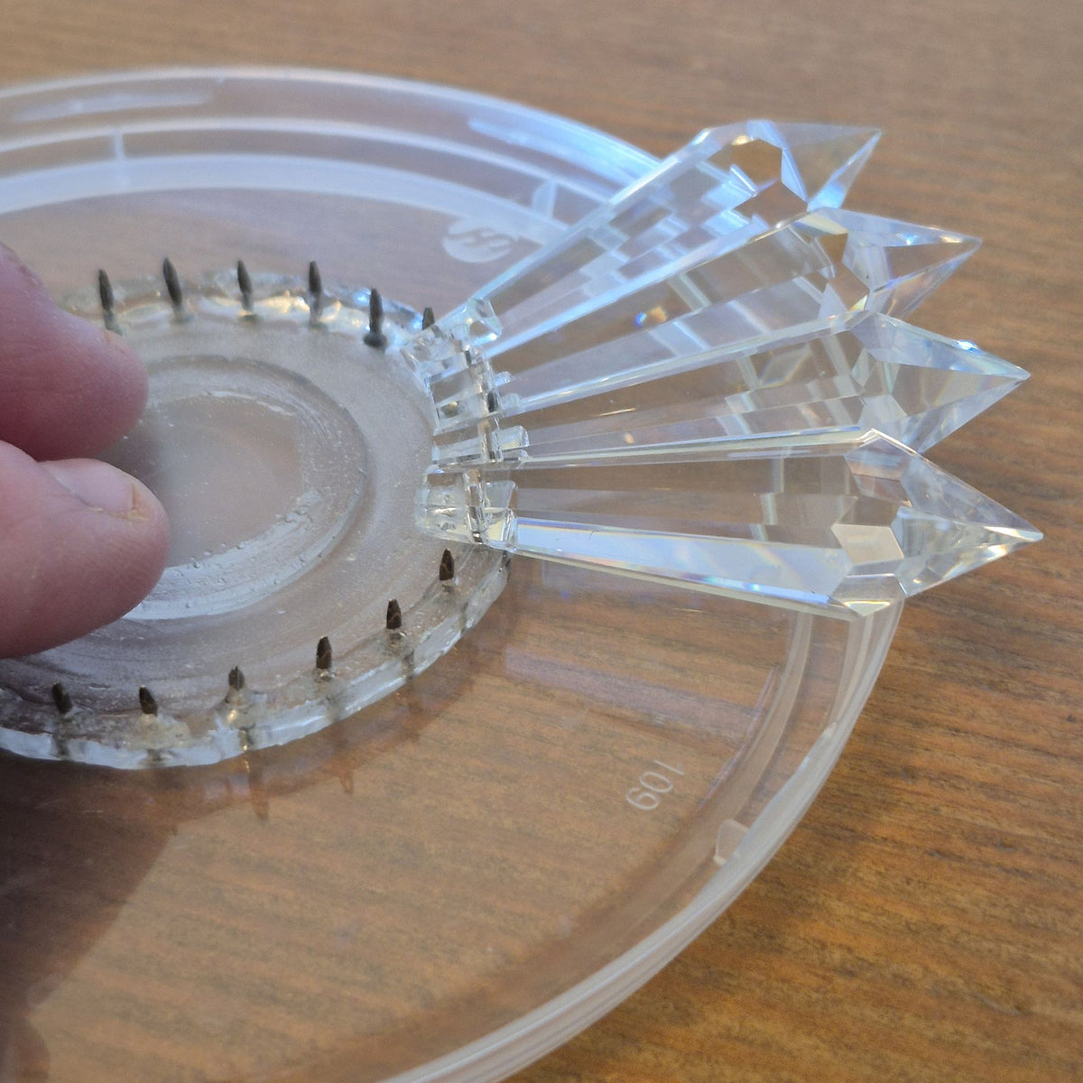 Close-up of a hand positioning Asfour crystal prisms around the clear resin center of a SunRain prism suncatcher kit.