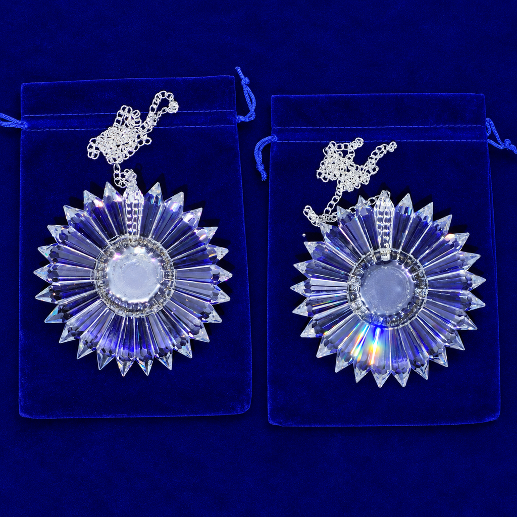 Two matching clear faceted crystal sunburst pendants with silver chains, displayed on blue velvet pouches against a dark blue background.