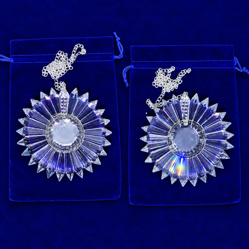Two matching clear faceted crystal sunburst pendants with silver chains, displayed on blue velvet pouches against a dark blue background.