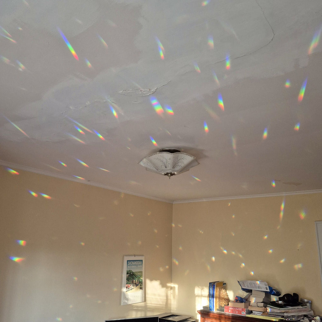 dozens of rainbow spectra cover walls and ceiling of room because of prism suncatchers hanging in the sunny window