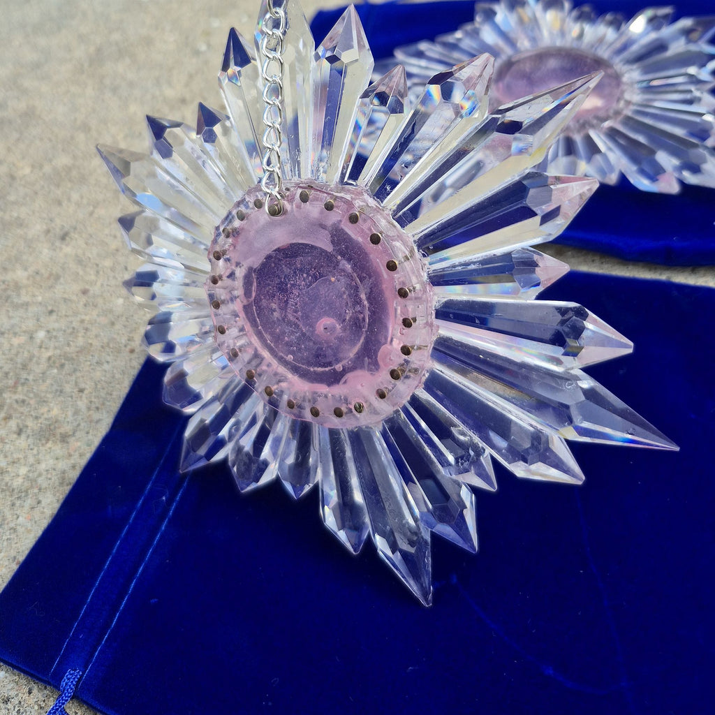 glass bubble disk over transparent pink center of two star-shaped prism suncatchers resting on blue pouches in the daylight