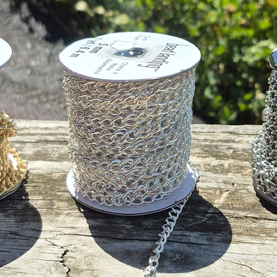 a spool of silver colored chain resting in sunny spot on wooden rail