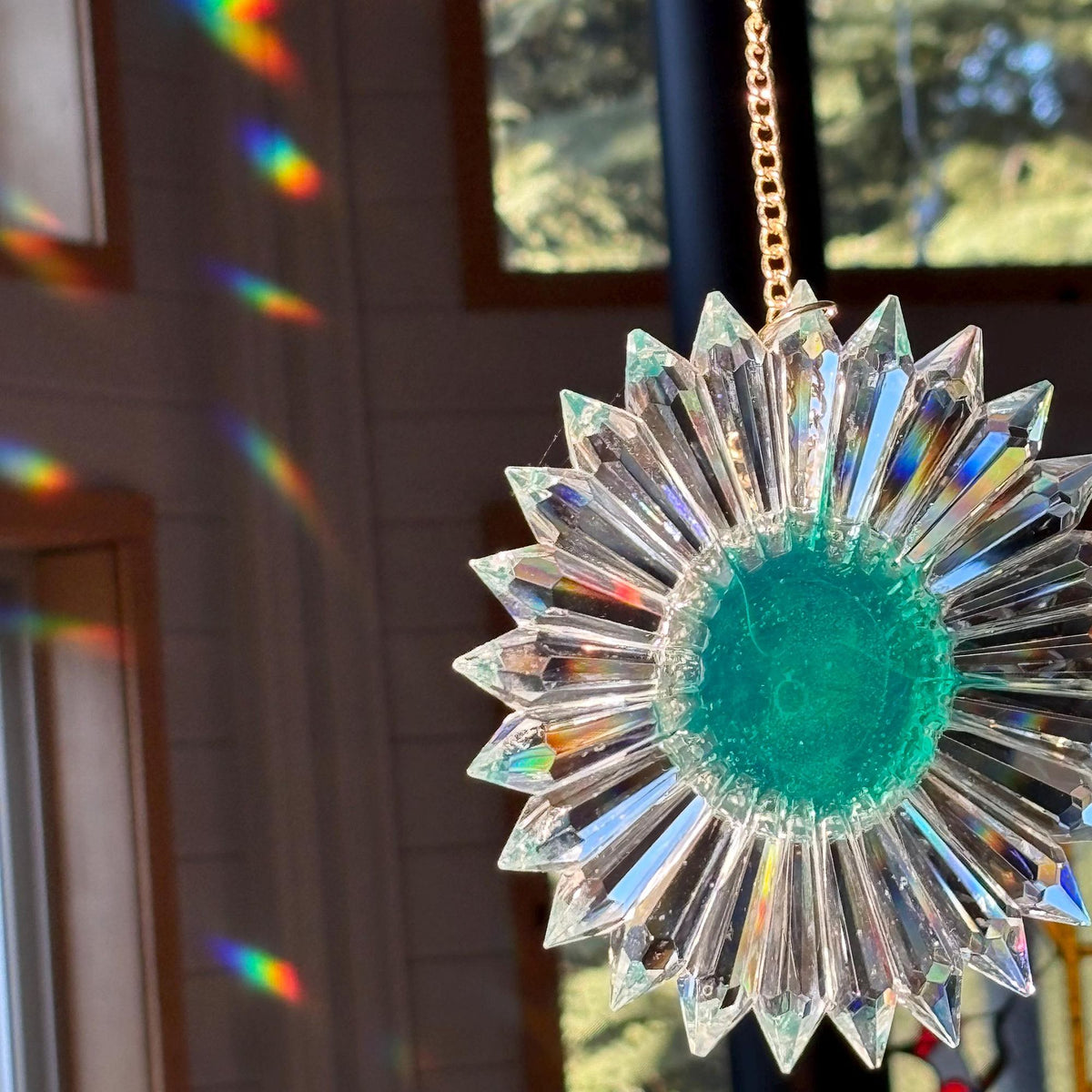 a green tinted prism suncatcher hanging in the sun from a gold colored chain