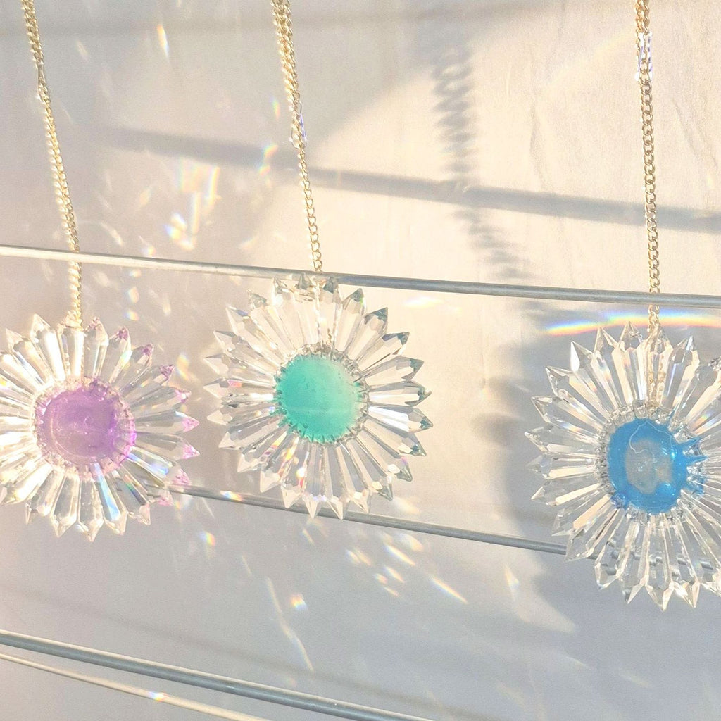 three 6-inch prism suncatchers on a rack in bright light: their centers are transparent pink, green and blue