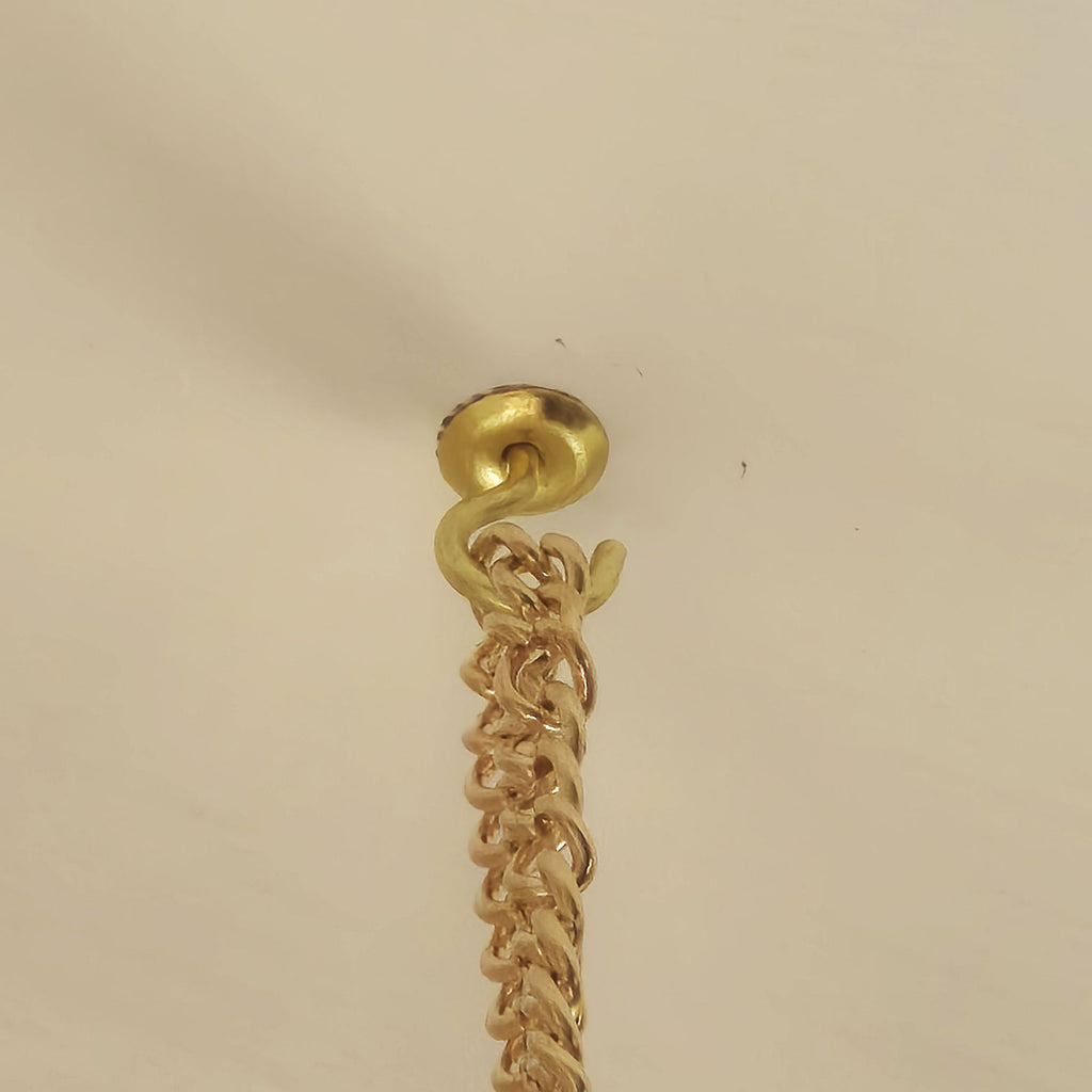 A close-up of a gold-toned chain hanging from a matching gold-toned wall hook or ceiling mount against a plain off-white background.