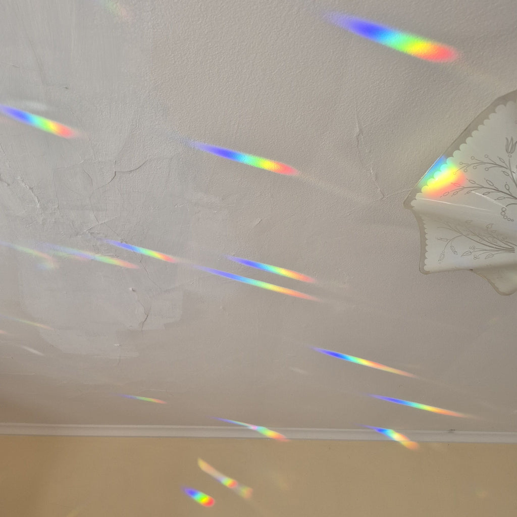 A white textured ceiling with multiple colorful rainbow light beams stretching across the surfaces.