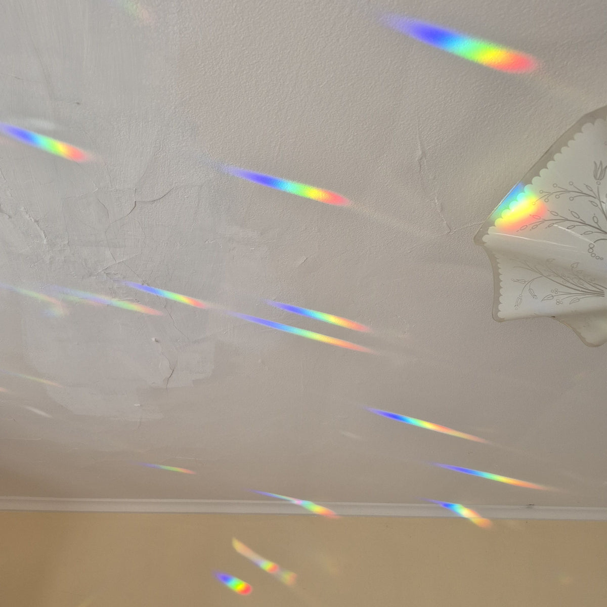A white textured ceiling with multiple colorful rainbow light beams stretching across the surfaces.