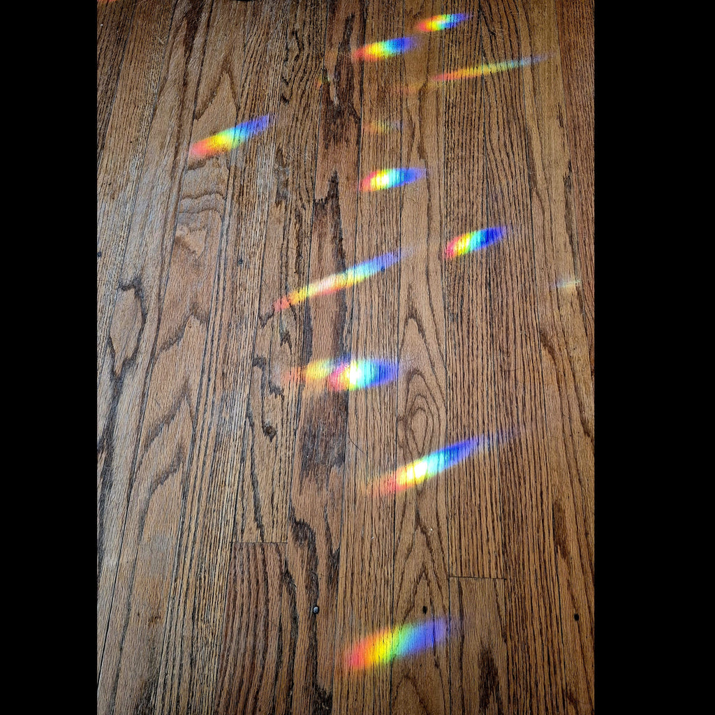 A close-up of a brown wood floor with several rainbow light refraction bars stretched and scattered across the surface.