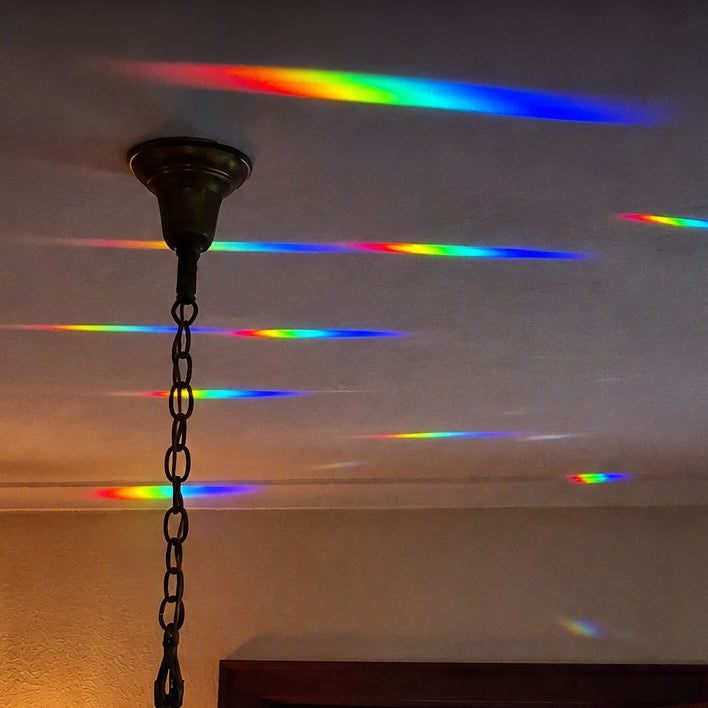 A hanging light fixture with a dark metal chain and canopy, shown in a room with rainbow-colored light beams projected across a ceiling and wall.