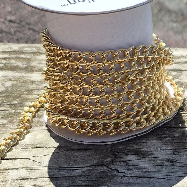a spool of gold colored chain resting on a wood rail in the sunshine