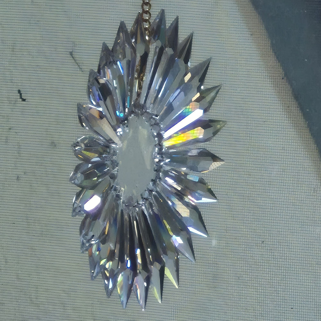 Oblique view of faceted crystal sun prism with a central resin well and radiating pointed crystal prisms, hanging against a textured gray fabric background.