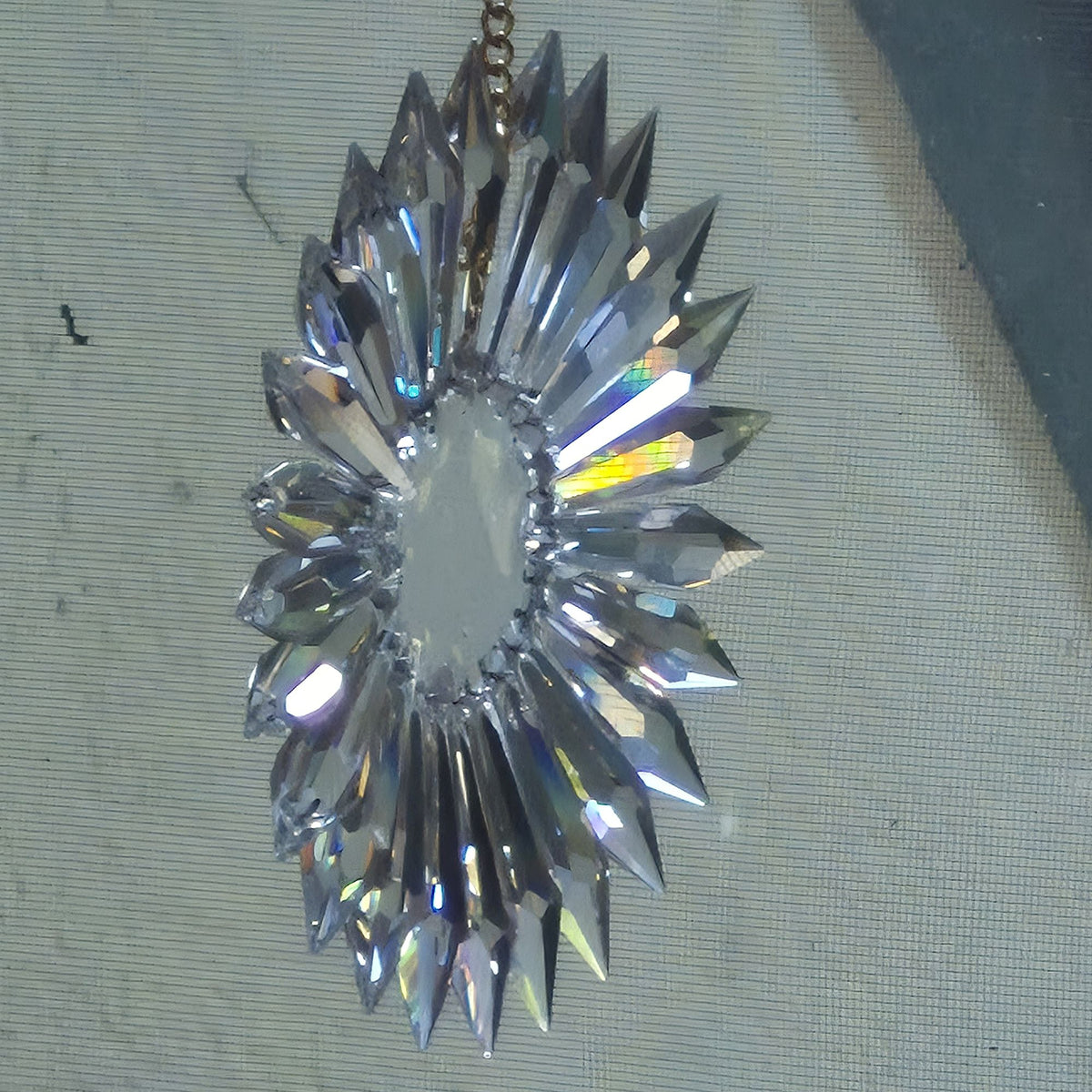 Oblique view of faceted crystal sun prism with a central resin well and radiating pointed crystal prisms, hanging against a textured gray fabric background.