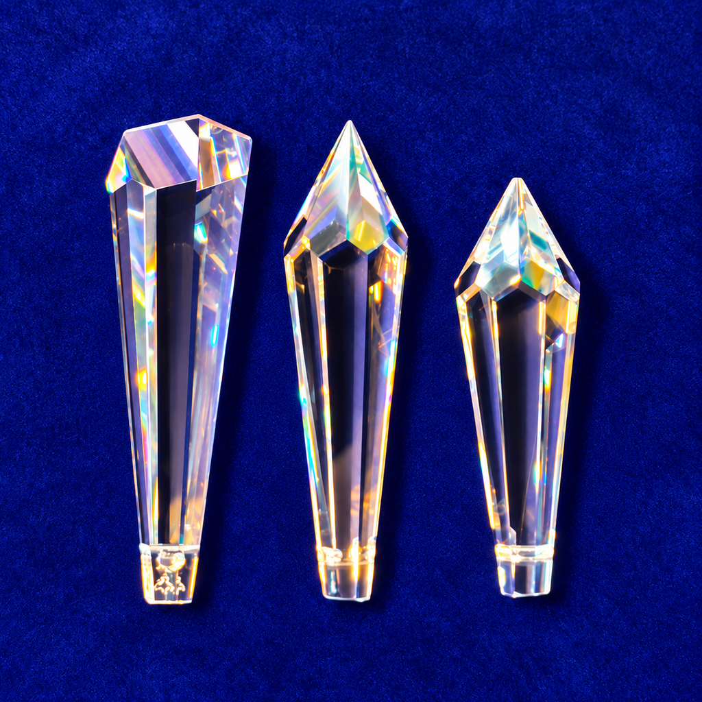 Three faceted clear crystal point prisms of different sizes arranged vertically on a textured dark blue background.