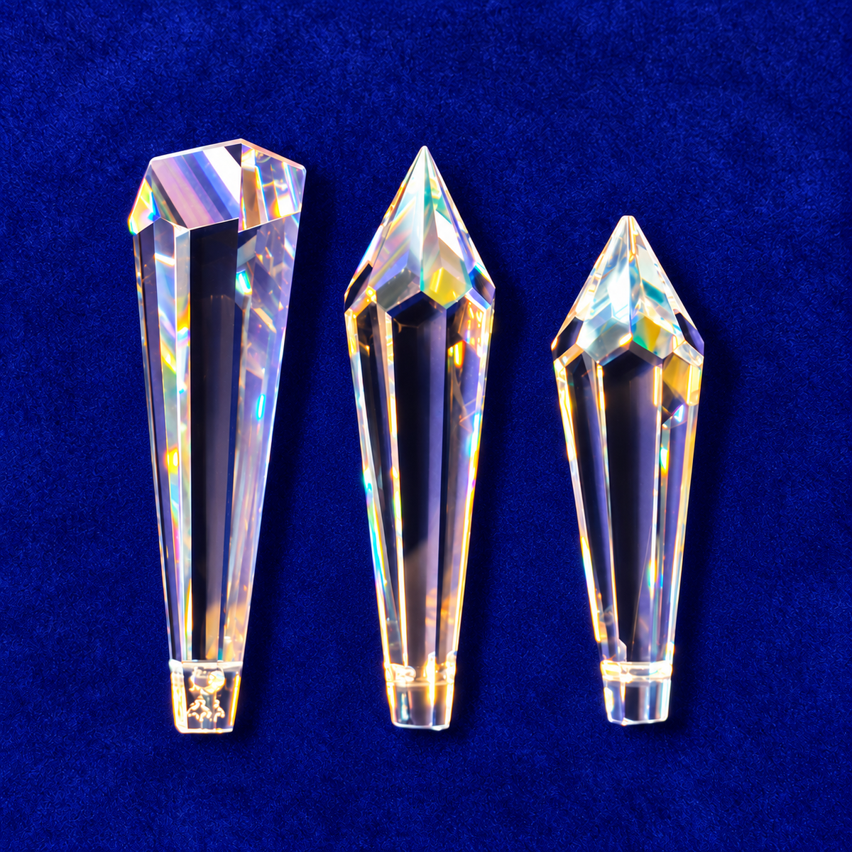 Three faceted clear crystal point prisms of different sizes arranged vertically on a textured dark blue background.