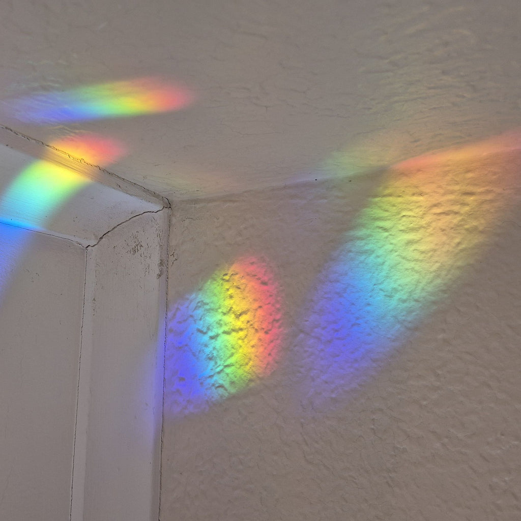 A corner of a textured white wall and ceiling illuminated by multiple rainbow light beams reflecting across the surfaces.