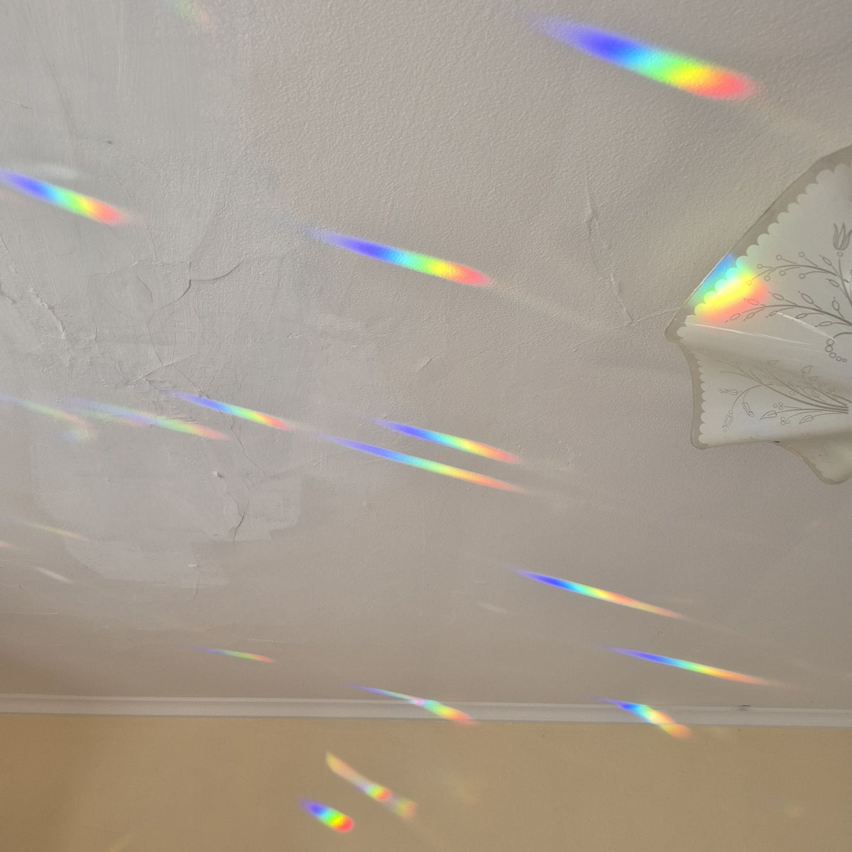 A white textured ceiling with multiple rainbow holographic light streaks reflecting across it, alongside a white decorative lamp shade.